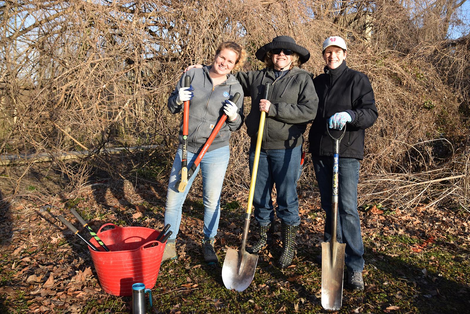 A group of three women standing holding gardening tools such as shovels