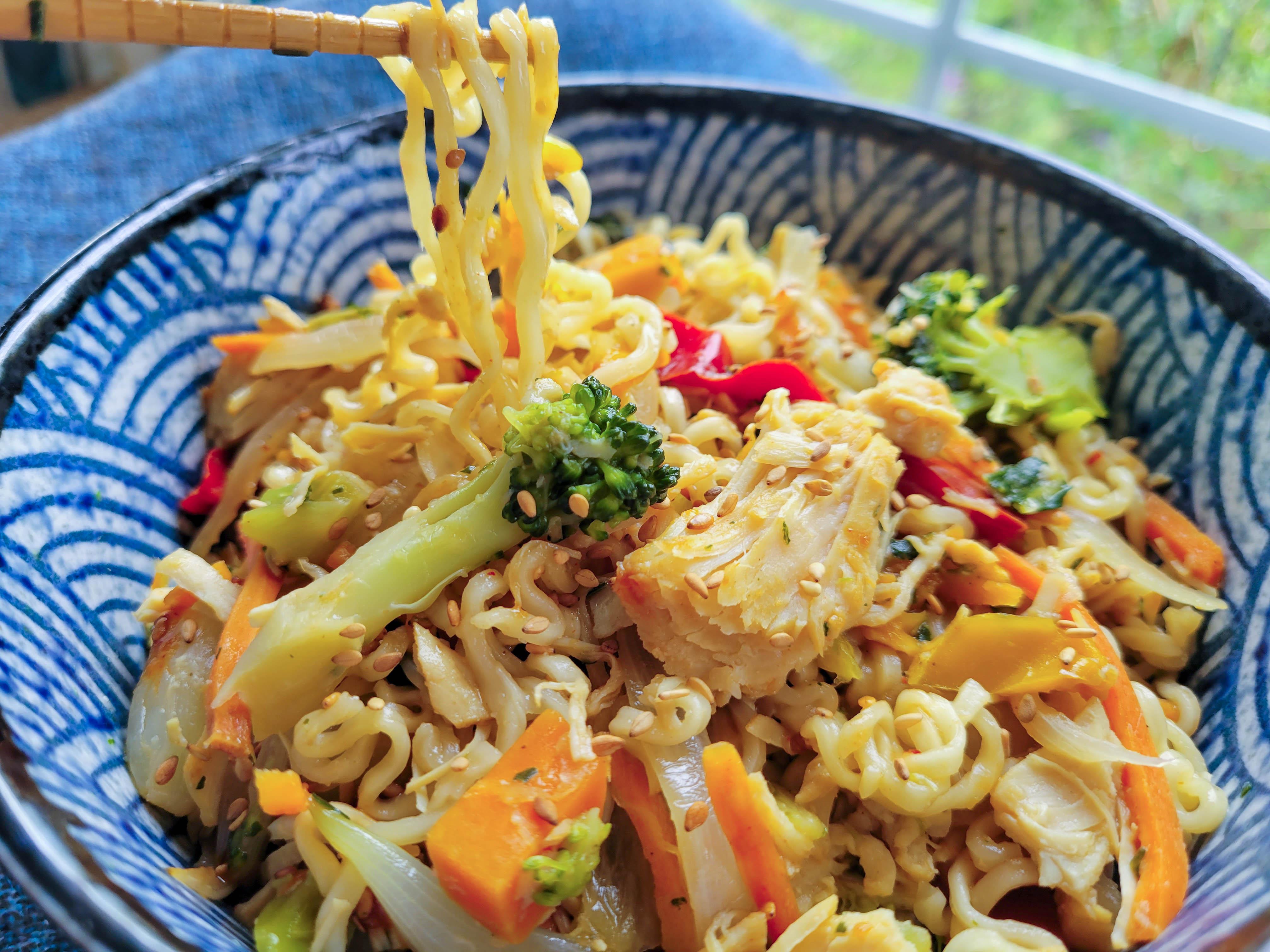 Ramen noodles with carrots, broccoli and onions in a blue bowl.