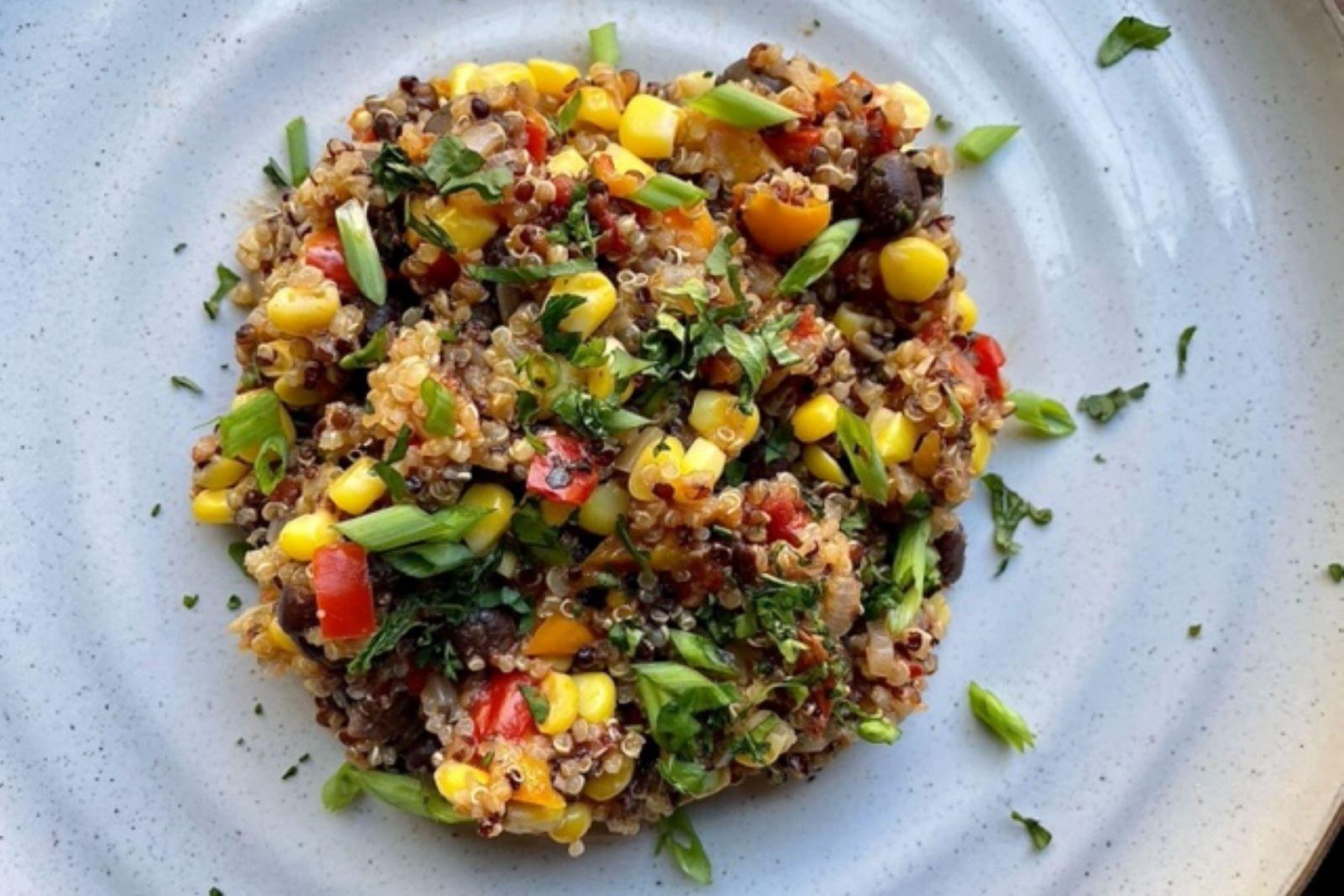 Quinoa with corn, peppers, black beans, and green onions and garnished with cilantro on a white plate.