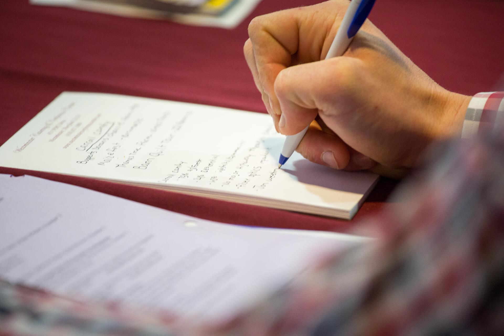 Picture of a person's hand using a pen to write on their pad of notebook paper