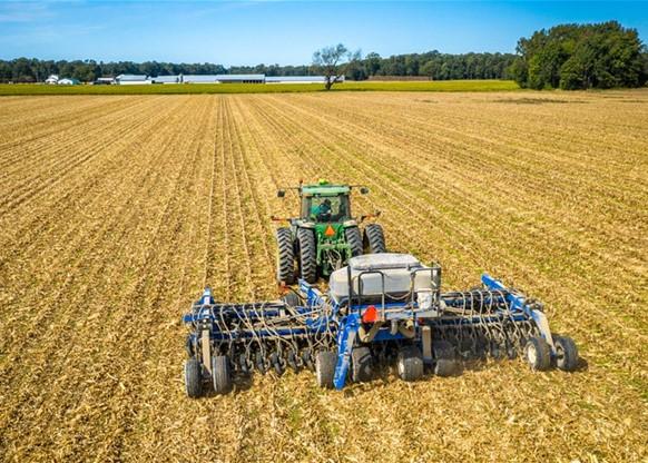 Tractor pulling farm equipment on harvested corn field.