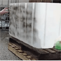 A person spraying black paint on the outside of the plastic container.