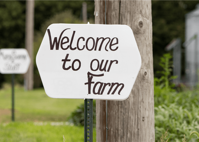 A sign at the edge of a farm that says, “Welcome to our farm”.