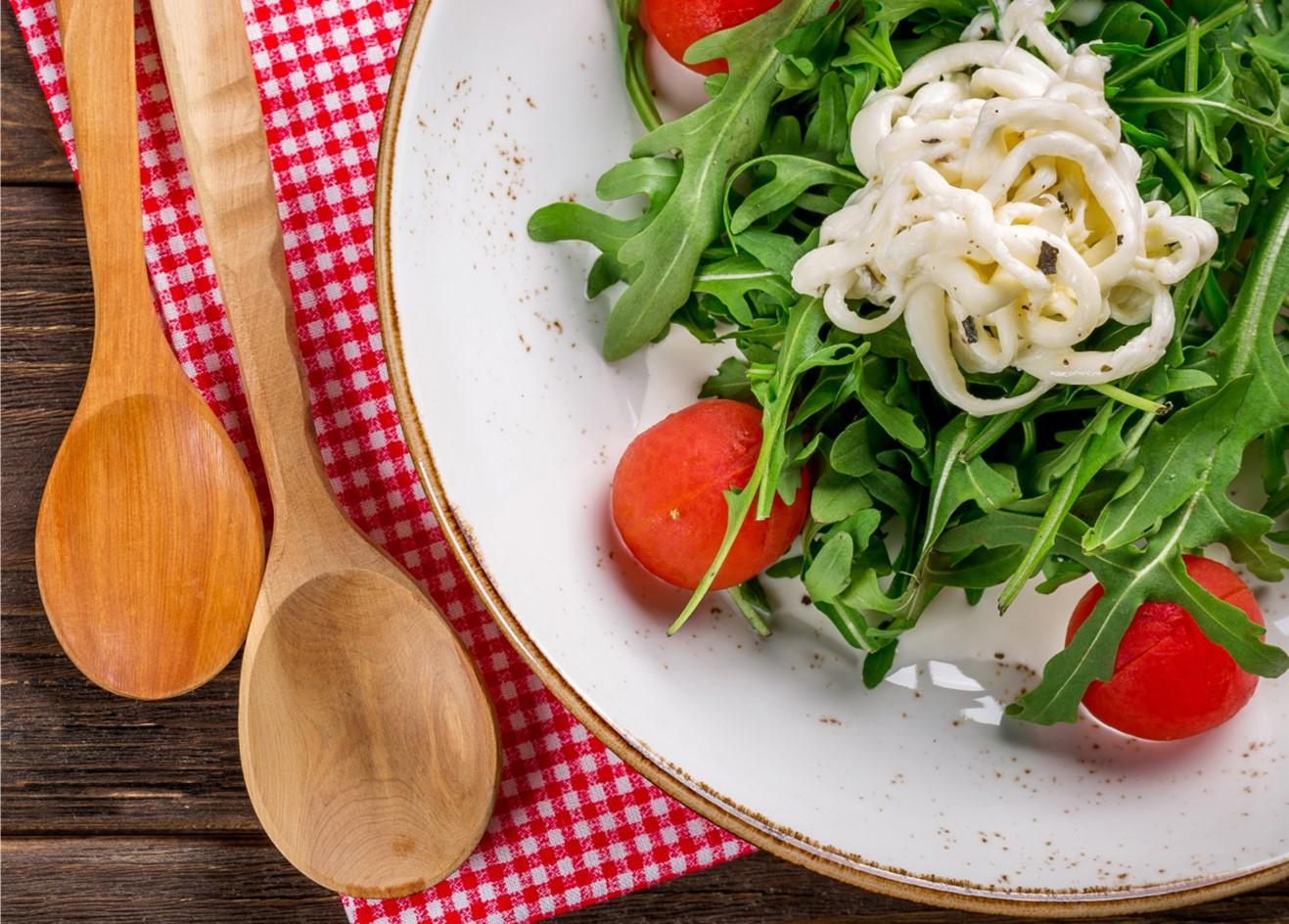 A plate of salad sitting on red checked table cloth and two wooden spoons