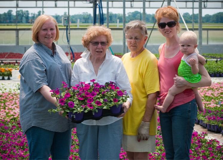 Farm women posing for picture in their greenhouse holding a flat of flowers