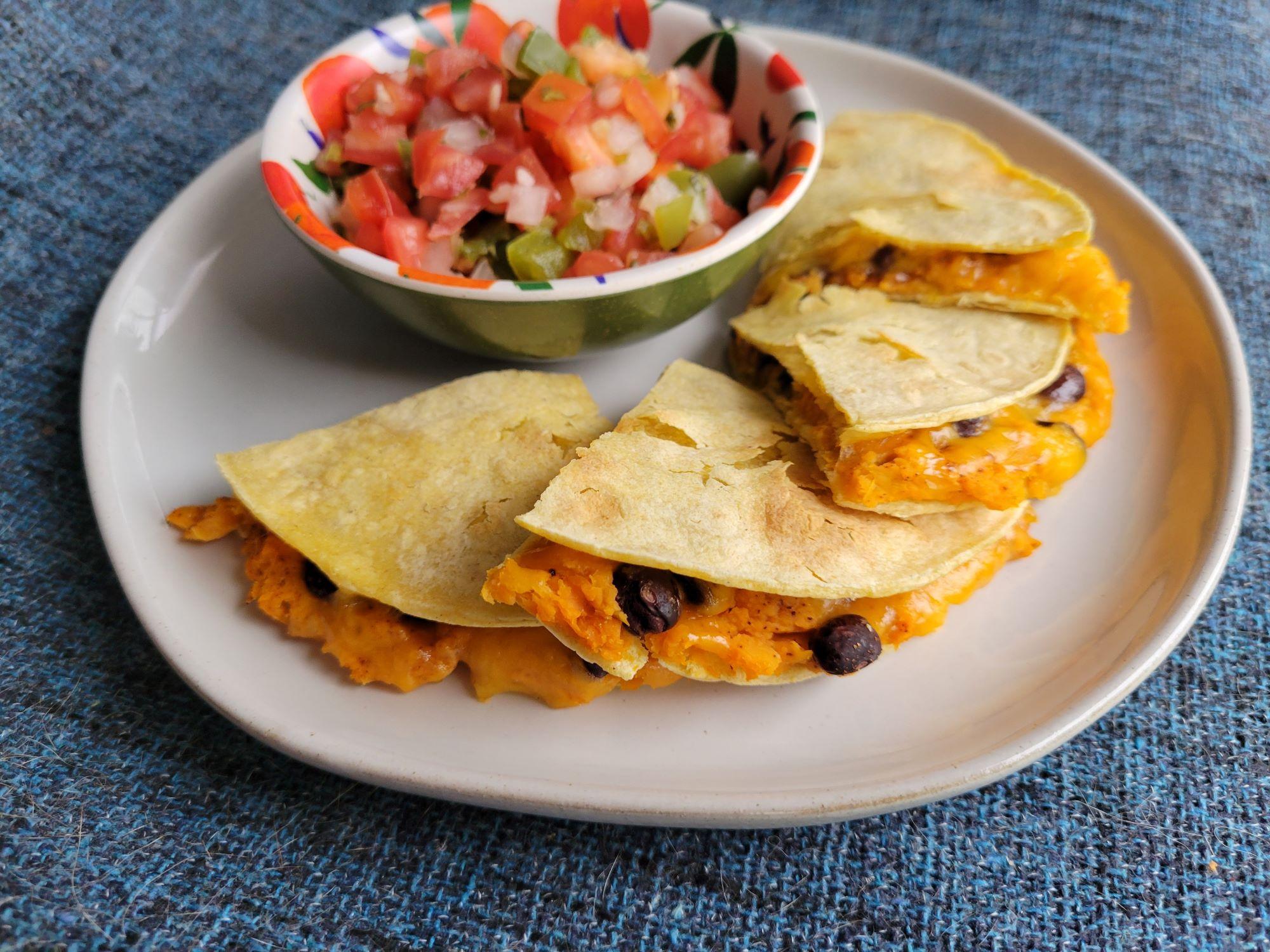 A quesadilla filled with sweet potato, black beans, and cheese and homemade pico de gallo on the side.