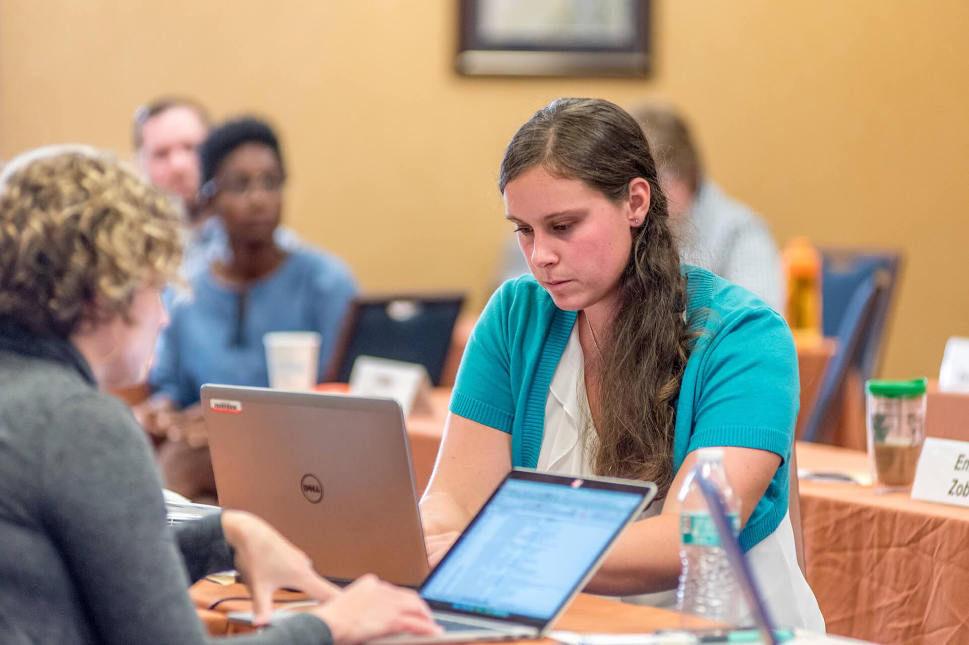 Woman in center of screen typing notes on a computer during a beginning farmer class