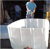 A person is using a water hose to clean the inside of a plastic container.