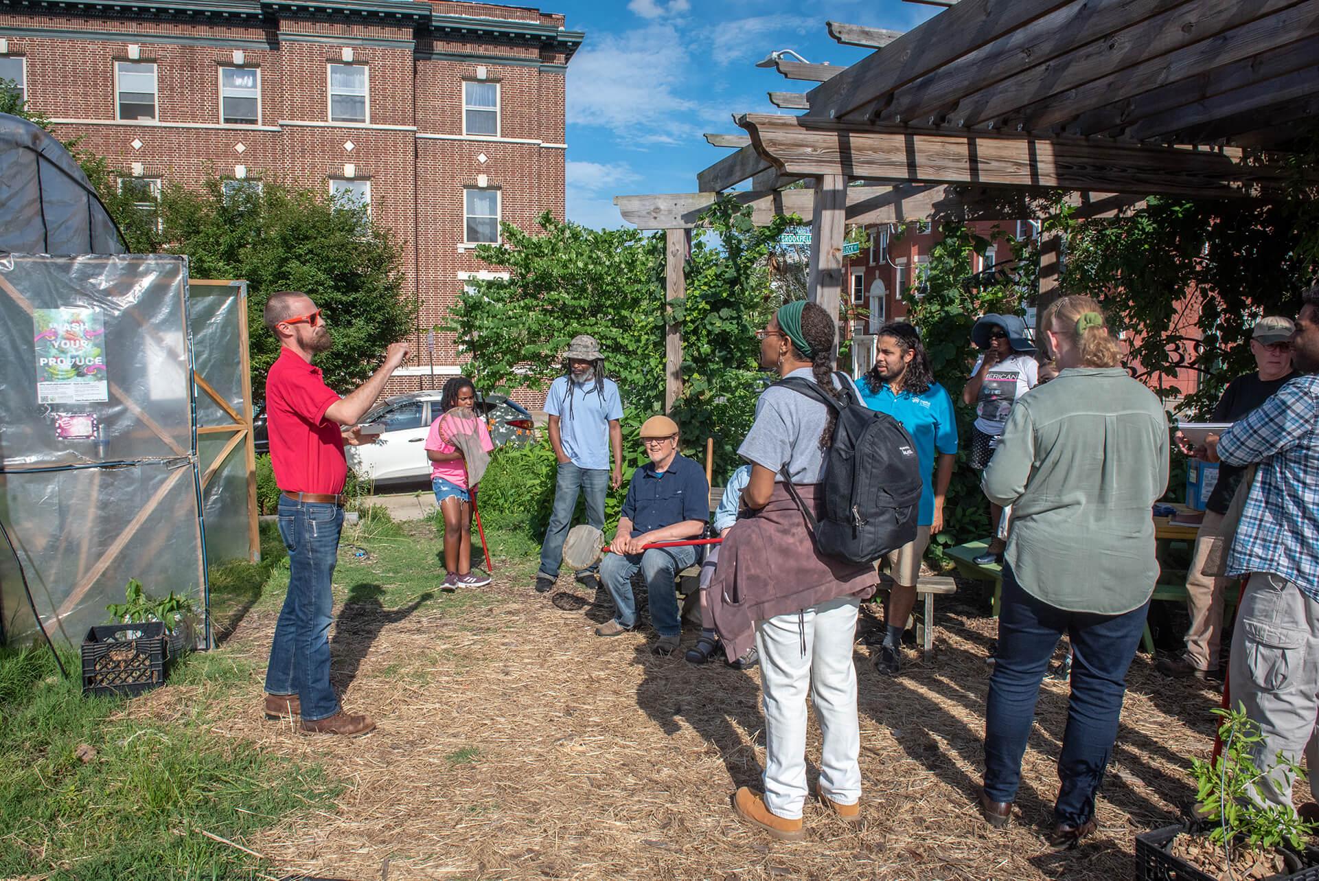 group of aspiring farmers standing in a circle listening to an extension agent on a community urban farm