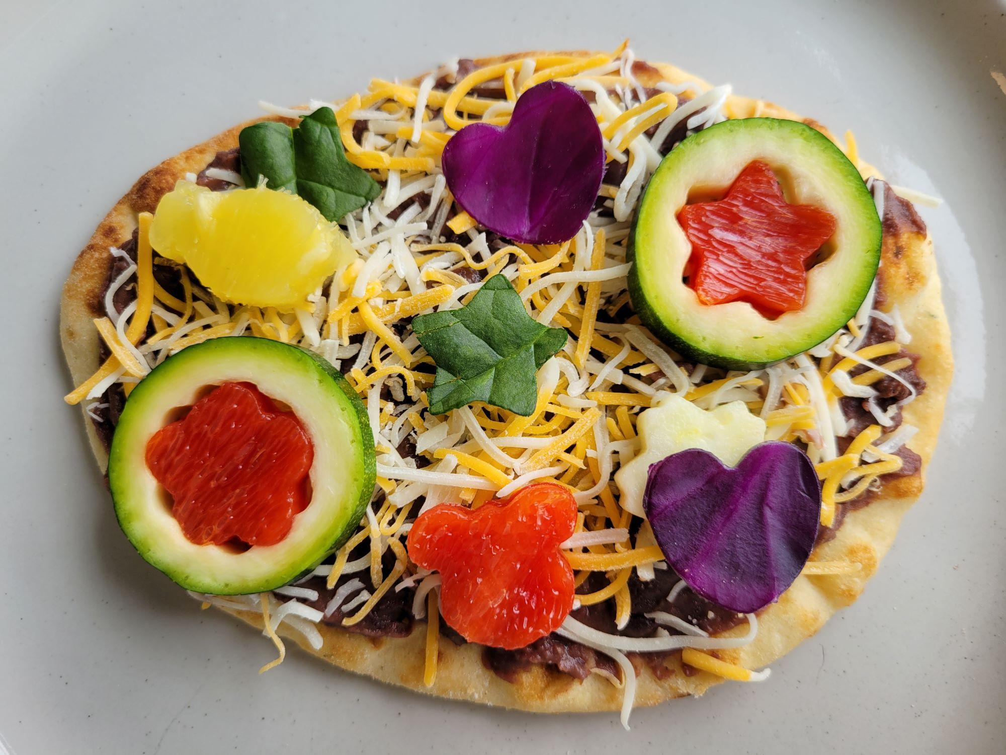 A flatbread with cheese and veggies cut into fun shapes.