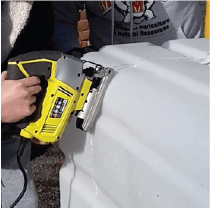 A person using a jigsaw to cut the plastic container along the marked line.