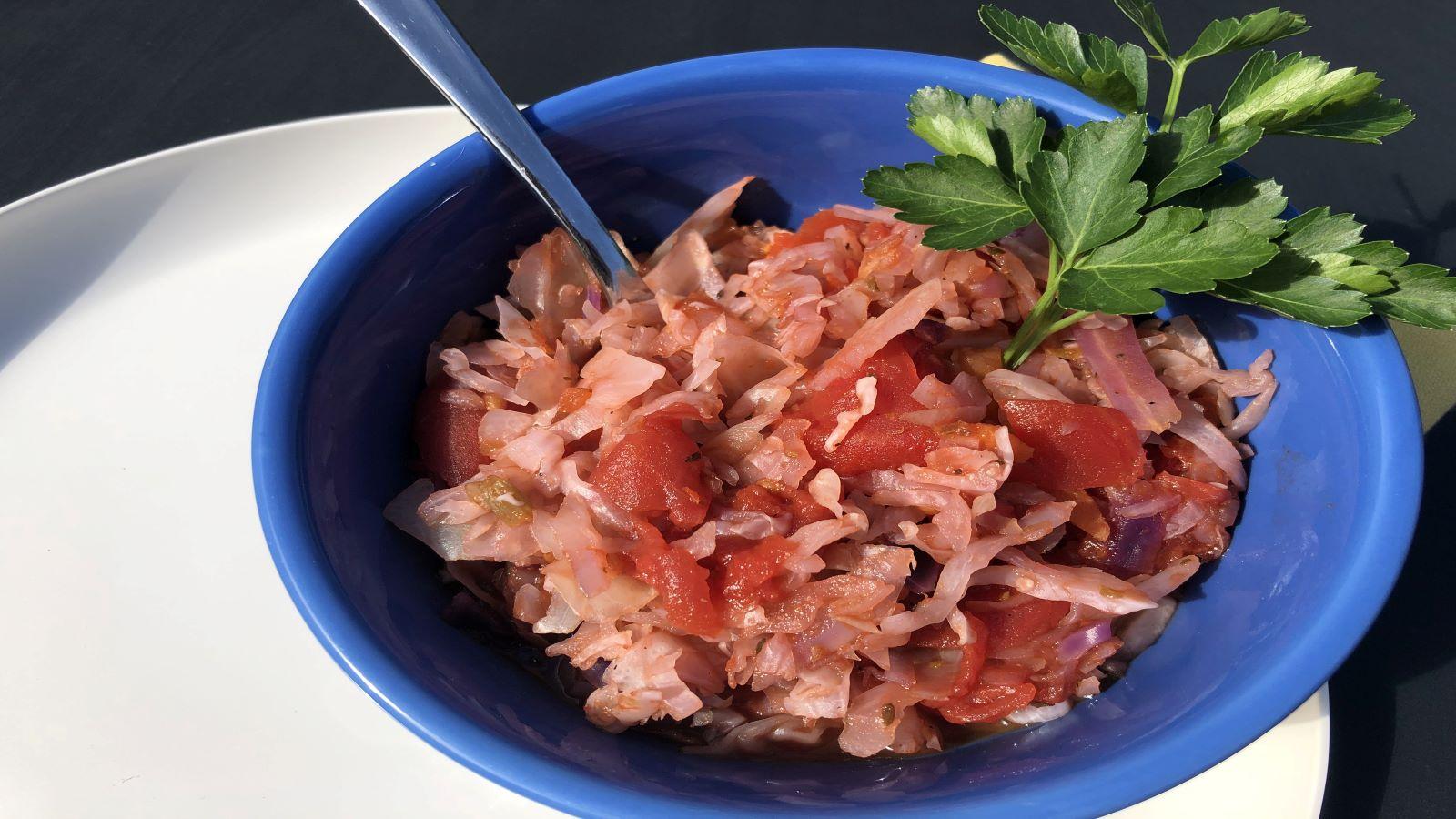 Shredded cabbage mixed with diced tomatoes and garnished with parsley in a blue bowl. 