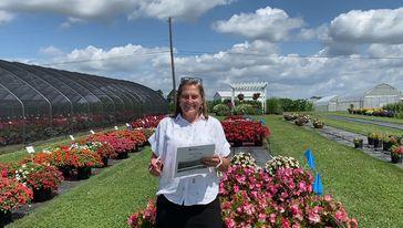 woman in white shirt outdoors with rows of annual flowers in the background