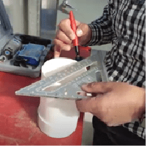  A person using a carpenter triangle to mark 2.5 inches wide by one-inch high windows on a four-inch PVC pipe.